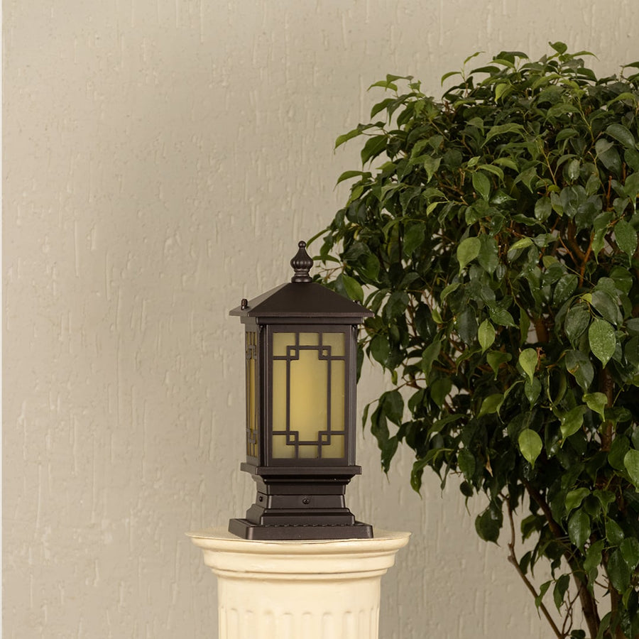 Black post light ribbed glass Light On placed next to a large green plant Lifestyle image for patio decor.