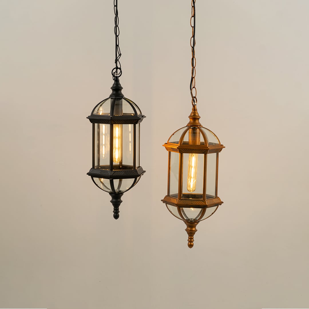 Two elongated outdoor lantern lights in black and antique brass finishes hanging together with warm filament bulbs glowing brightly.