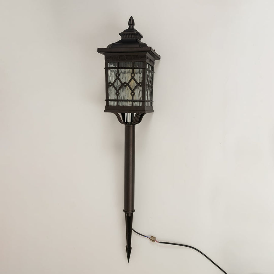 Black metal garden spike lantern with patterned glass shown with light off on a white background showcasing its detailed frame and tall spike base.