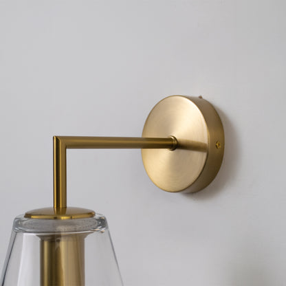 Modern brass wall light with clear cone glass shade and sleek metallic arm for luxury interiors.