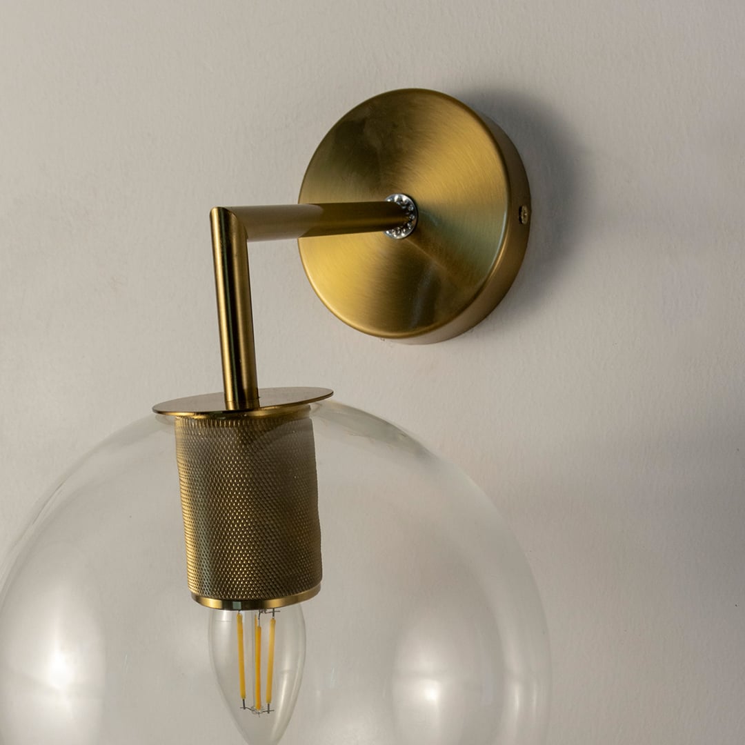 Closeup of gold wall light with clear glass globe and metal holder showing fine detailing and contemporary style.
