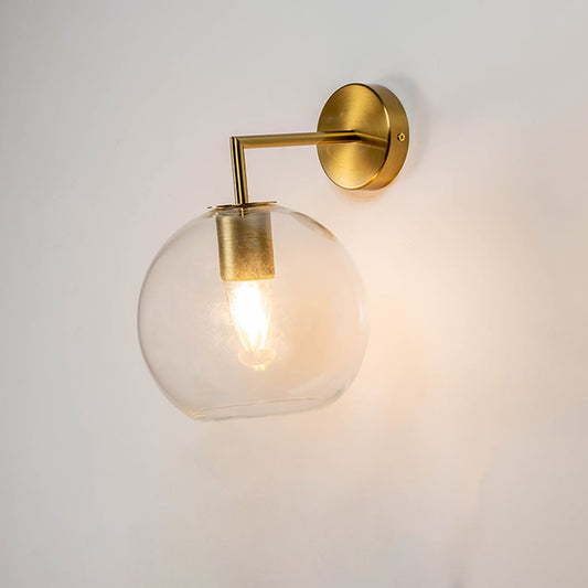 Modern gold metal wall light with warm glowing glass shade for luxury bedroom living room and hallway home decor spaces.