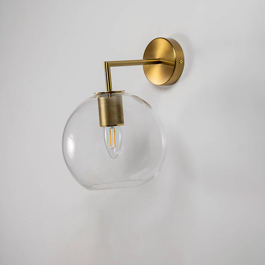 Gold wall light with clear glass globe displayed off on white background ideal for luxury and minimalist interiors.