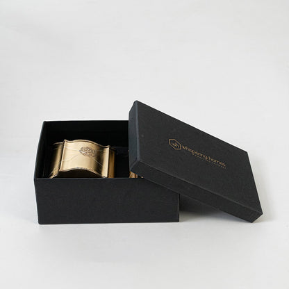 Gold metal pen holders set with scalloped edges and engraved crest displayed side by side on white background.