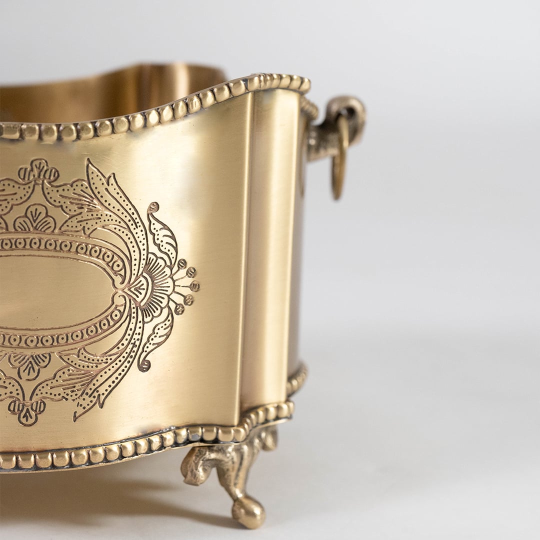 A closeup view of the brass champagne bucket focusing on its embossed floral emblem smooth metal texture and detailed beaded edges with elegant craftsmanship.