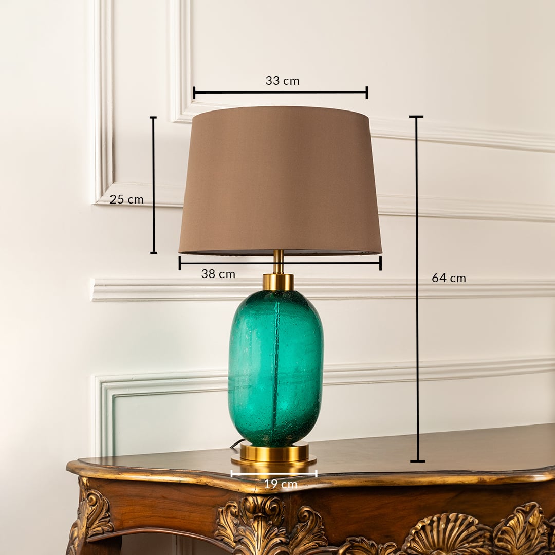Teal glass table lamp with brown shade with size 64cm height and 31cm width on carved console table with light off for modern stylish décor.