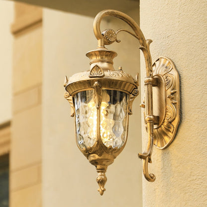 A gold antique wall lantern with the light on illuminating the exterior wall and casting a warm glow across the entrance creating an elegant and inviting outdoor ambiance.
