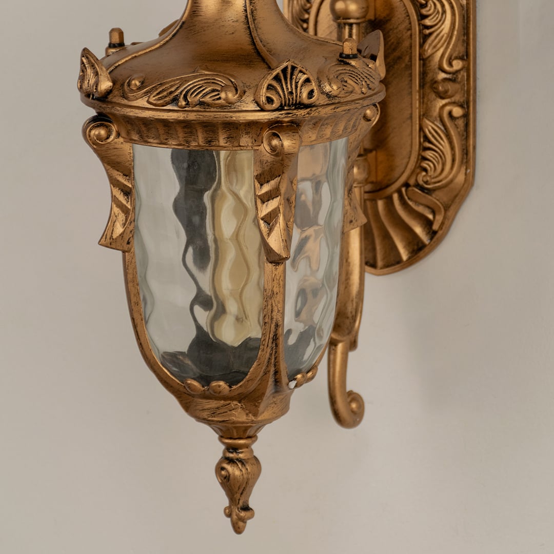 A closeup of the gold antique lantern showing the hammered glass warm glowing bulb and carved frame detailing that adds a luxurious classic style to the exterior.