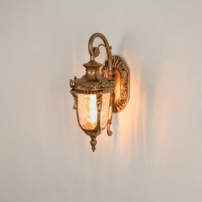 Antique brass metal outdoor wall light on white background with ornate scroll accents and clear glass shade for decor.