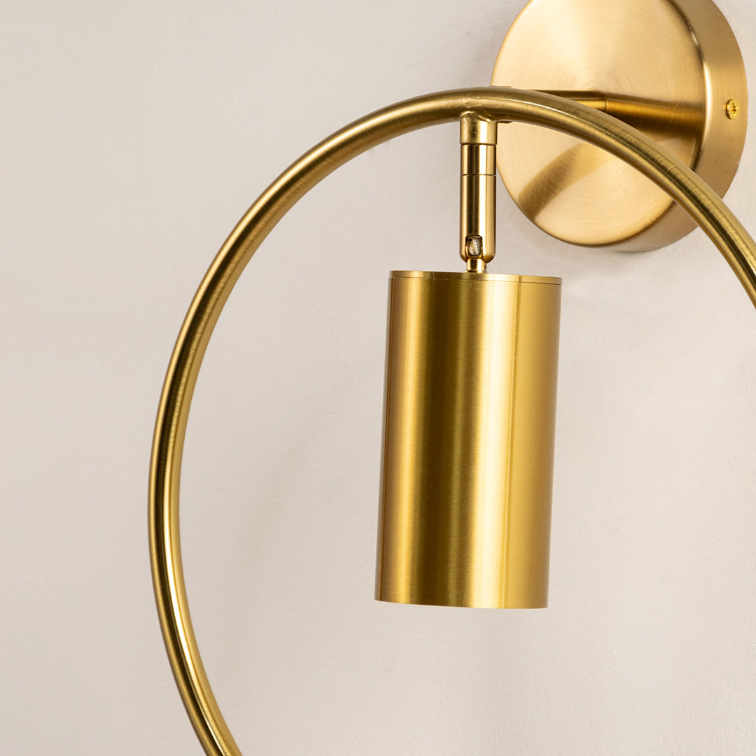 Closeup of gold metal wall light with curved arm and cylindrical shade showcasing sleek finish for modern interior decor styling.