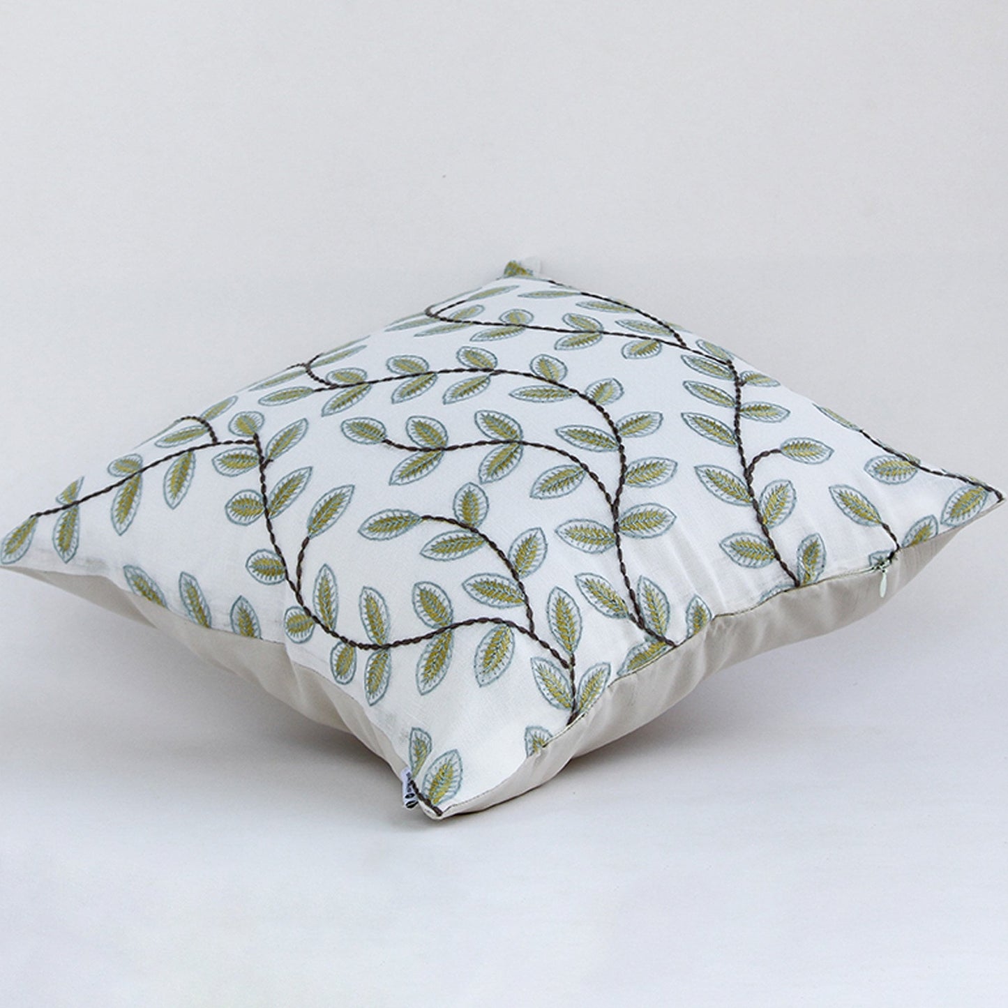 Soft cotton cushion cover with green leaf embroidery shown at an angle offering a fresh nature inspired décor accent with a breathable gentle and skin friendly fabric finish ideal for modern interiors.