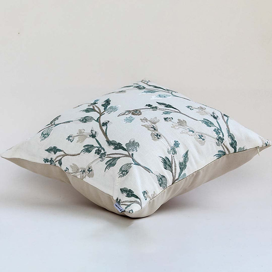 Soft white cotton cushion cover with teal botanical design placed at an angle offering a fresh natural décor touch with a breathable smooth and skin friendly fabric.