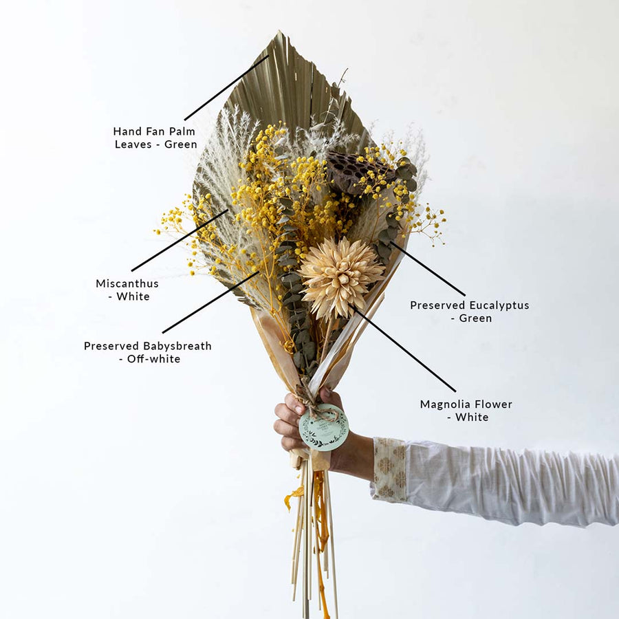 Hand holding a rustic dried floral bouquet with palm spear leaf and yellow fillers for tabletop vase on white background.