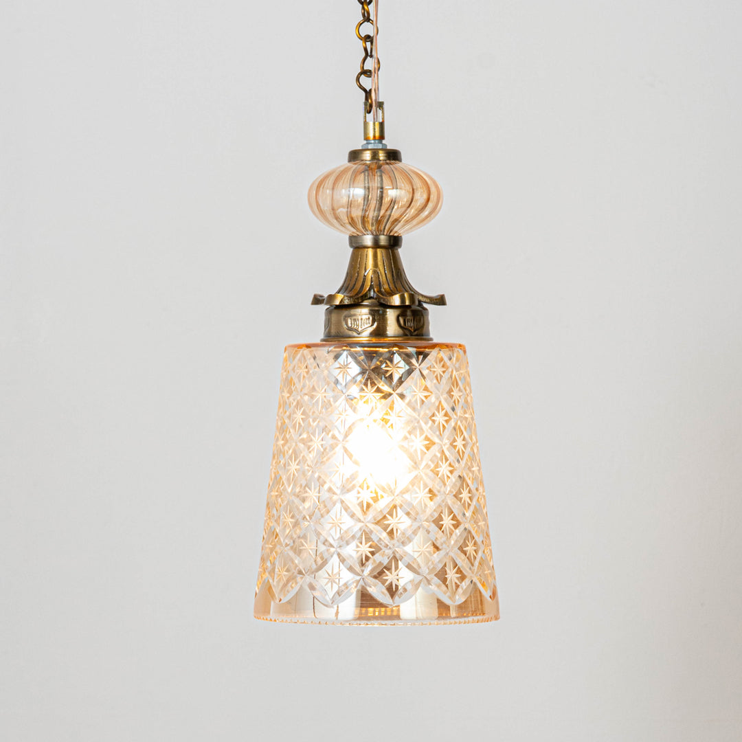 Decorative pendant light in gold metal finish with patterned glass shade for dining room or living decor lighting white background.
