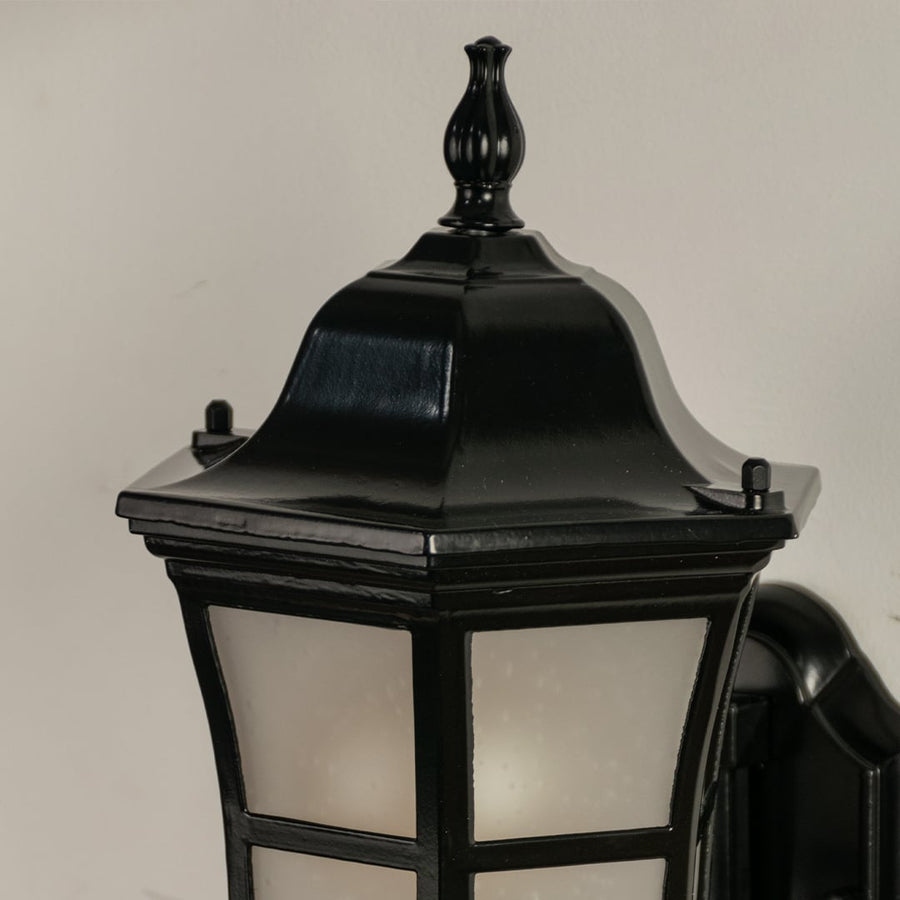 Closeup of black metal outdoor lantern showing frosted glass and elegant curved arm detail perfect for enhancing home entrance porch and patio Decor.