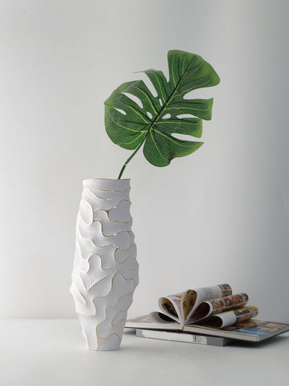 Tall white ceramic vase with textured design styled with green leaf placed on table beside open magazine.