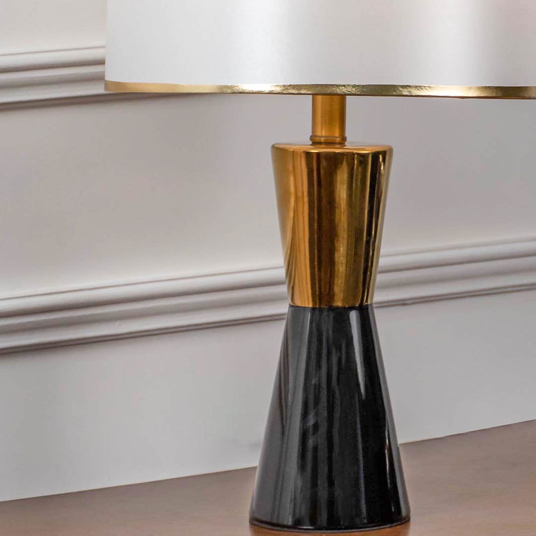 Closeup of black ceramic table lamp with gold accents and fabric drum shade for contemporary home decor.