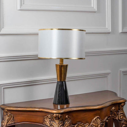 Black and gold ceramic table lamp turned off with drum shade and brass accents displayed on white background decor.