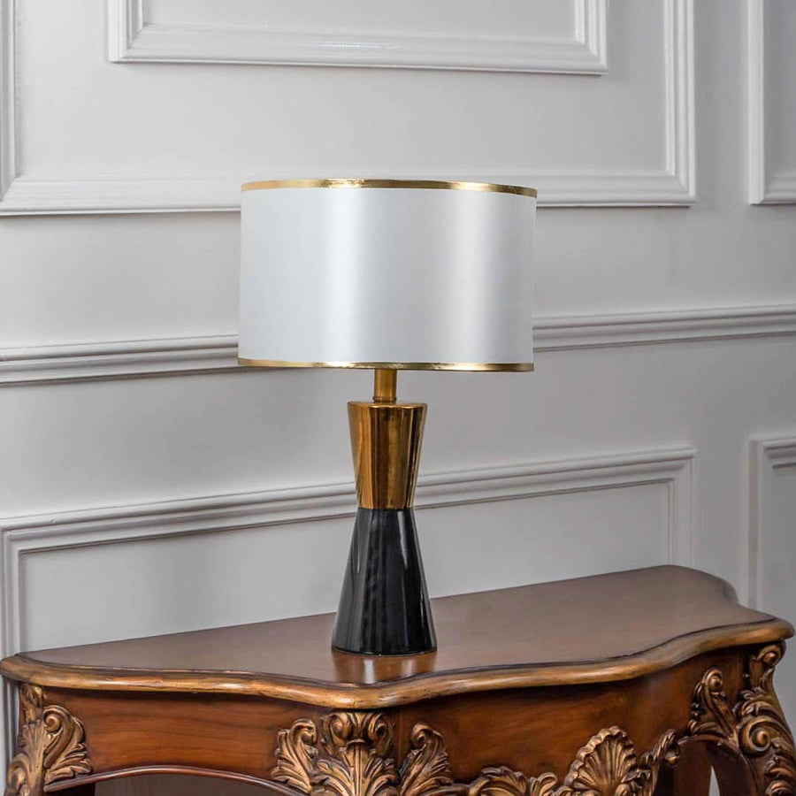 Black and gold ceramic table lamp turned off with drum shade and brass accents displayed on white background decor.