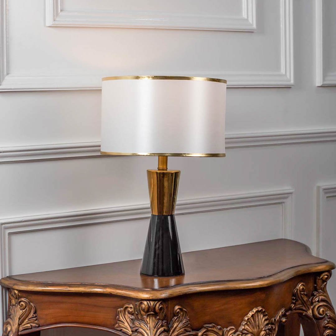 Modern table lamp with black and gold base and white fabric shade on wooden table elegant lighting for bedroom and living room decor.