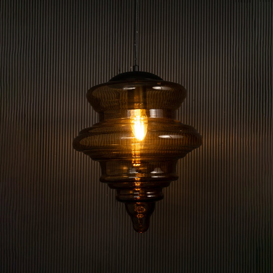 Elegant amber glass pendant hanging light illuminated on dark background highlighting its artistic craftsmanship and warm ambient glow.