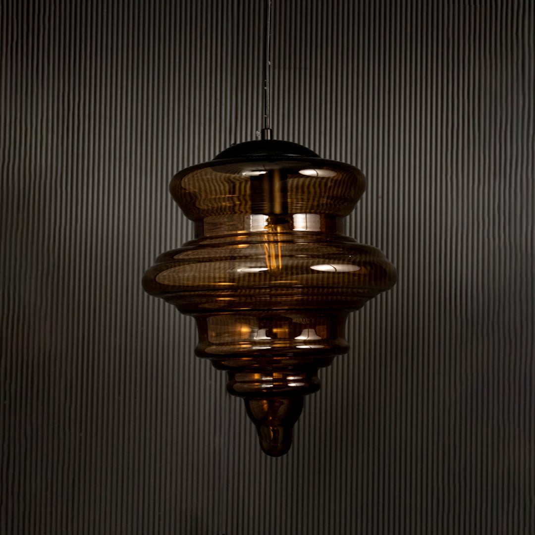 Amber glass pendant light displayed on dark background with lights off highlighting its glossy texture and sculptural design.