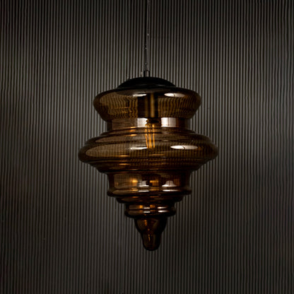 Amber glass pendant light displayed on dark background with lights off highlighting its glossy texture and sculptural design.