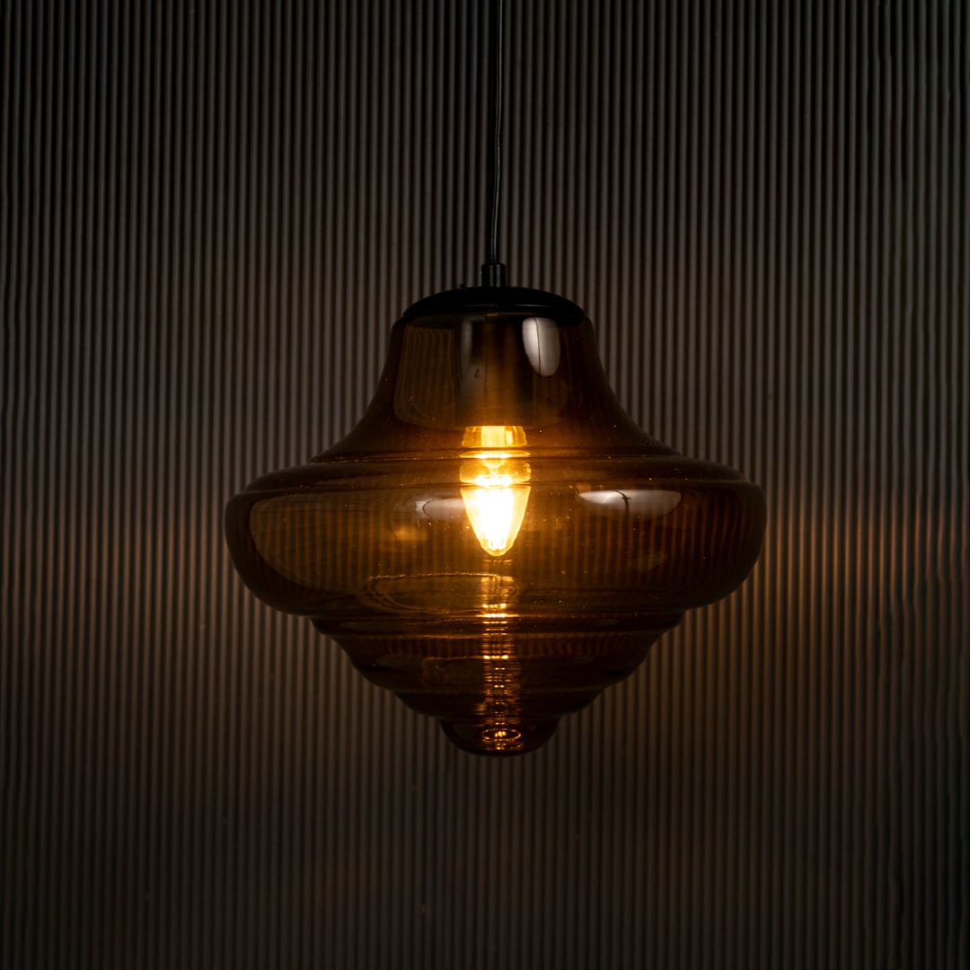 Elegant amber glass pendant hanging light illuminated on dark background highlighting glossy texture and warm ambient lighting style.