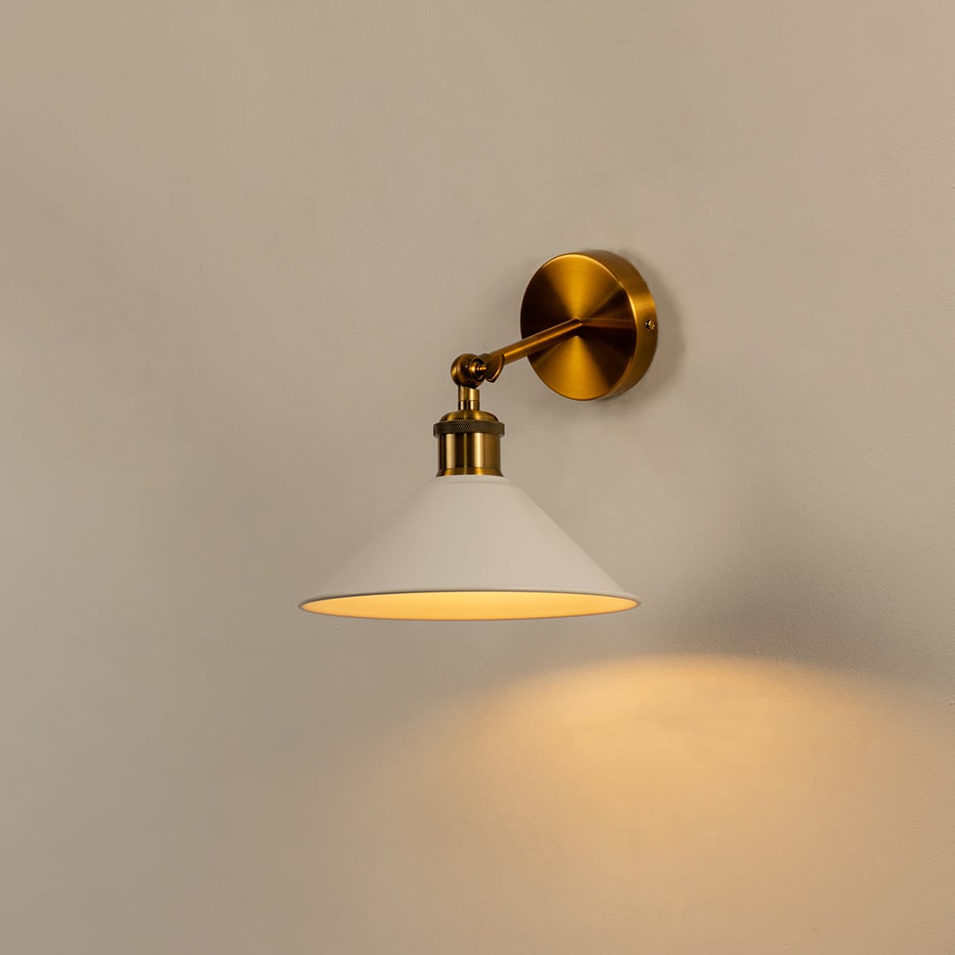 White cone wall light with brass fixture glowing warmly on white wall bringing modern elegance to minimalist interiors.