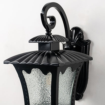 Closeup view of lantern outdoor wall light with curved arm scalloped metal top and frosted glass panels glowing softly.