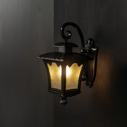 Black lantern outdoor wall light turned on highlights frosted textured glass against a dark background.