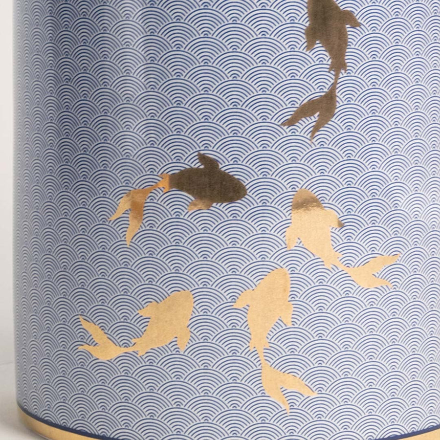 Closeup of blue ceramic jar with intricate golden fish design showcasing glossy finish and fine craftsmanship.