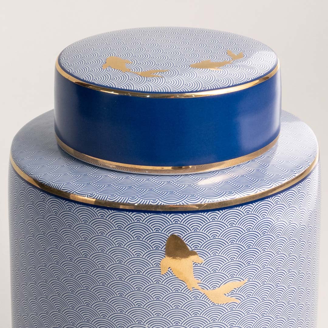 Closeup of blue ceramic jar with intricate golden fish design showcasing glossy finish and fine craftsmanship.