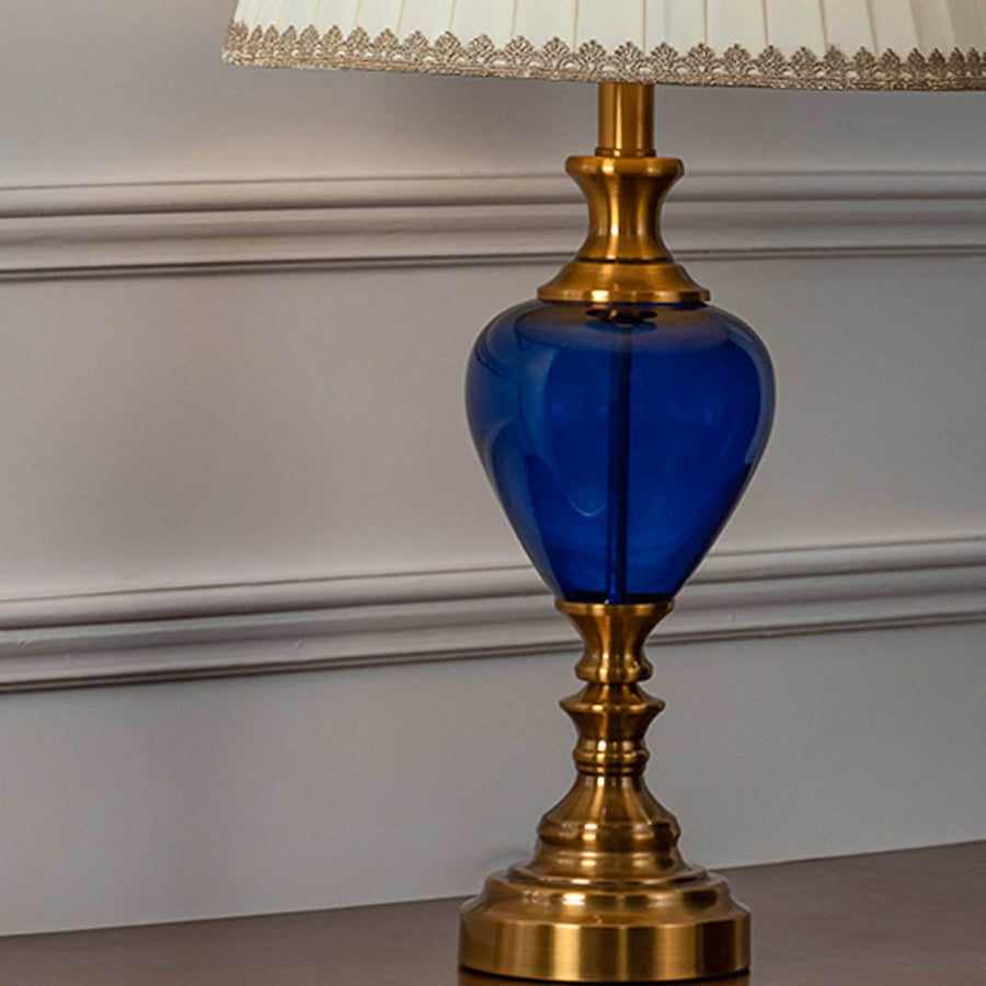 Closeup of blue glass table lamp with golden detailing and pleated lampshade showing elegant home decor style.
