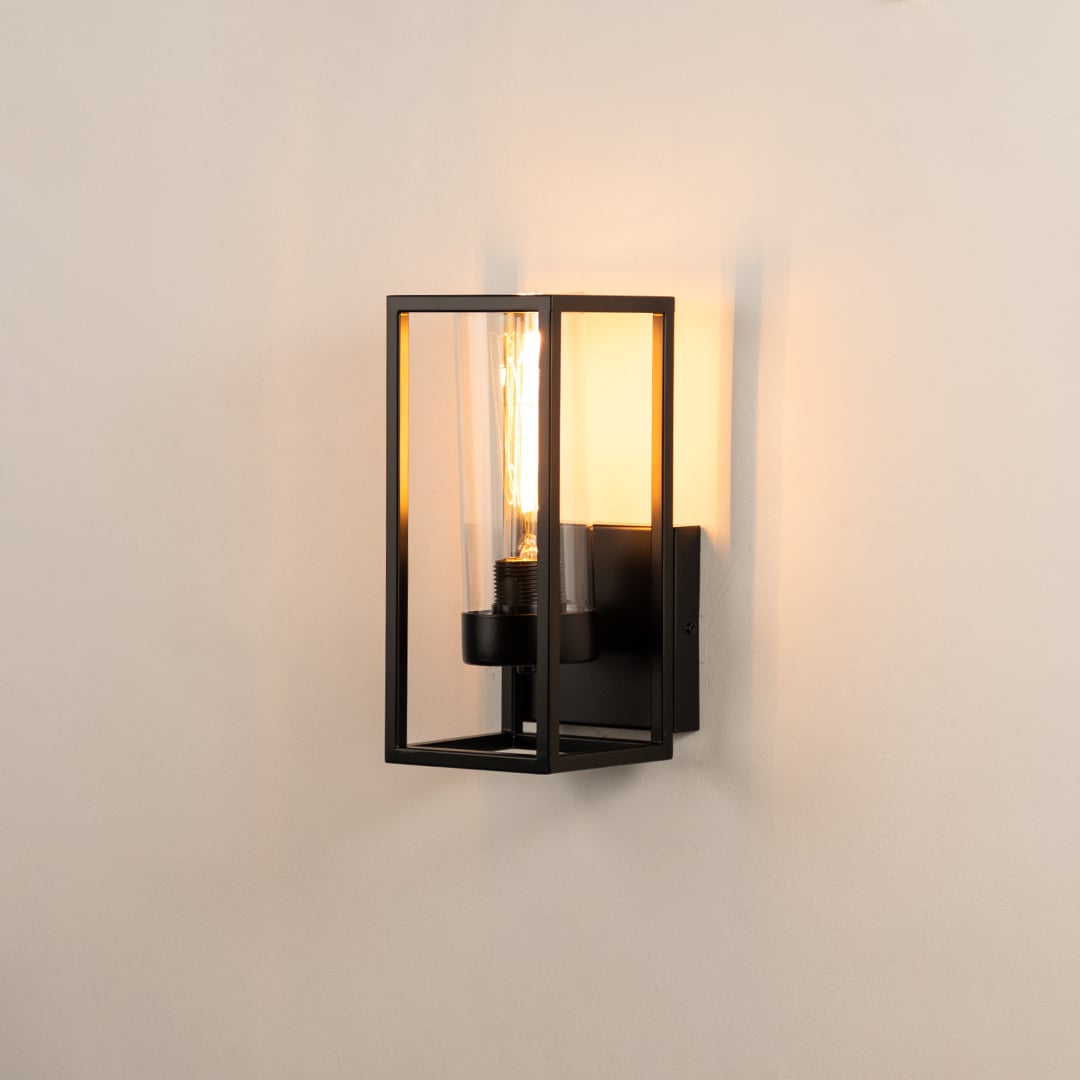 Closeup of black metal wall light with clear glass shade for modern hallway and luxury decor spaces.

