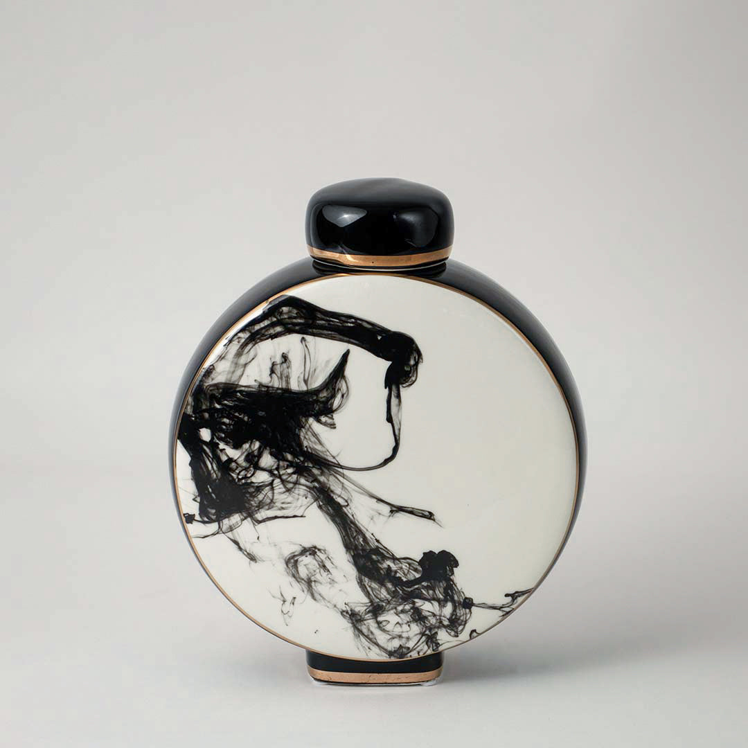 Round ceramic vase with black and white artistic pattern placed on wooden table against neutral wall background enhancing elegant decorative home accent appeal.