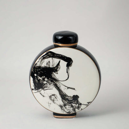 Round ceramic vase with black and white artistic pattern placed on wooden table against neutral wall background enhancing elegant decorative home accent appeal.