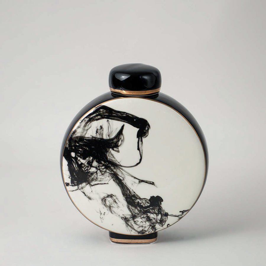 Round ceramic vase with black and white artistic pattern placed on wooden table against neutral wall background enhancing elegant decorative home accent appeal.