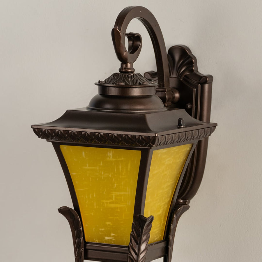 A closeup view of the bronze lantern showing the glowing yellow glass interior and ornate metal frame detailing that enhances the traditional design when the light is on.