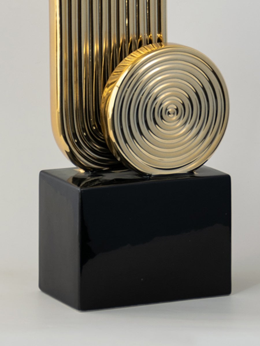 Detailed closeup of gold metal abstract sculpture with circular pattern on black base for modern interiors.