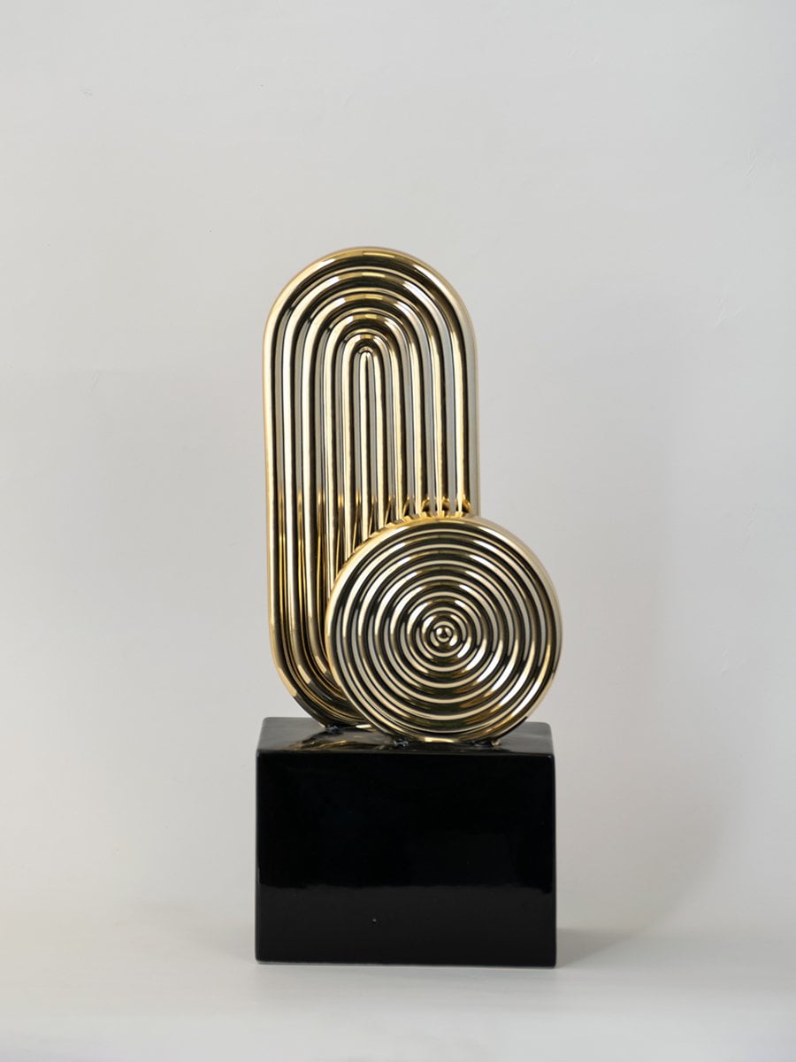 Gold metal decorative sculpture on black base for table placement with modern design on white background.