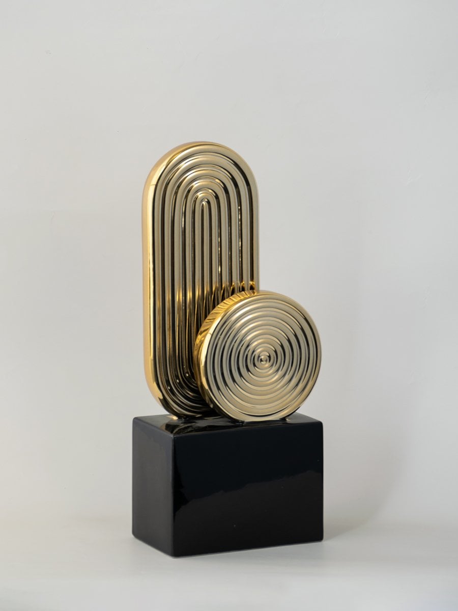 Gold metal abstract sculpture on black base modern home decor accent on white background.