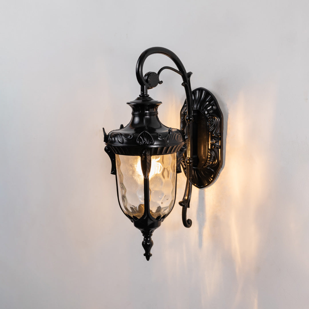 Glossy black metal outdoor wall light on white background with clear water glass shade casting reflections for decor.