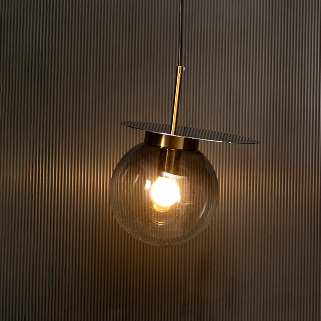 Elegant smoked glass pendant light illuminated on dark background highlighting refined craftsmanship and warm modern design.