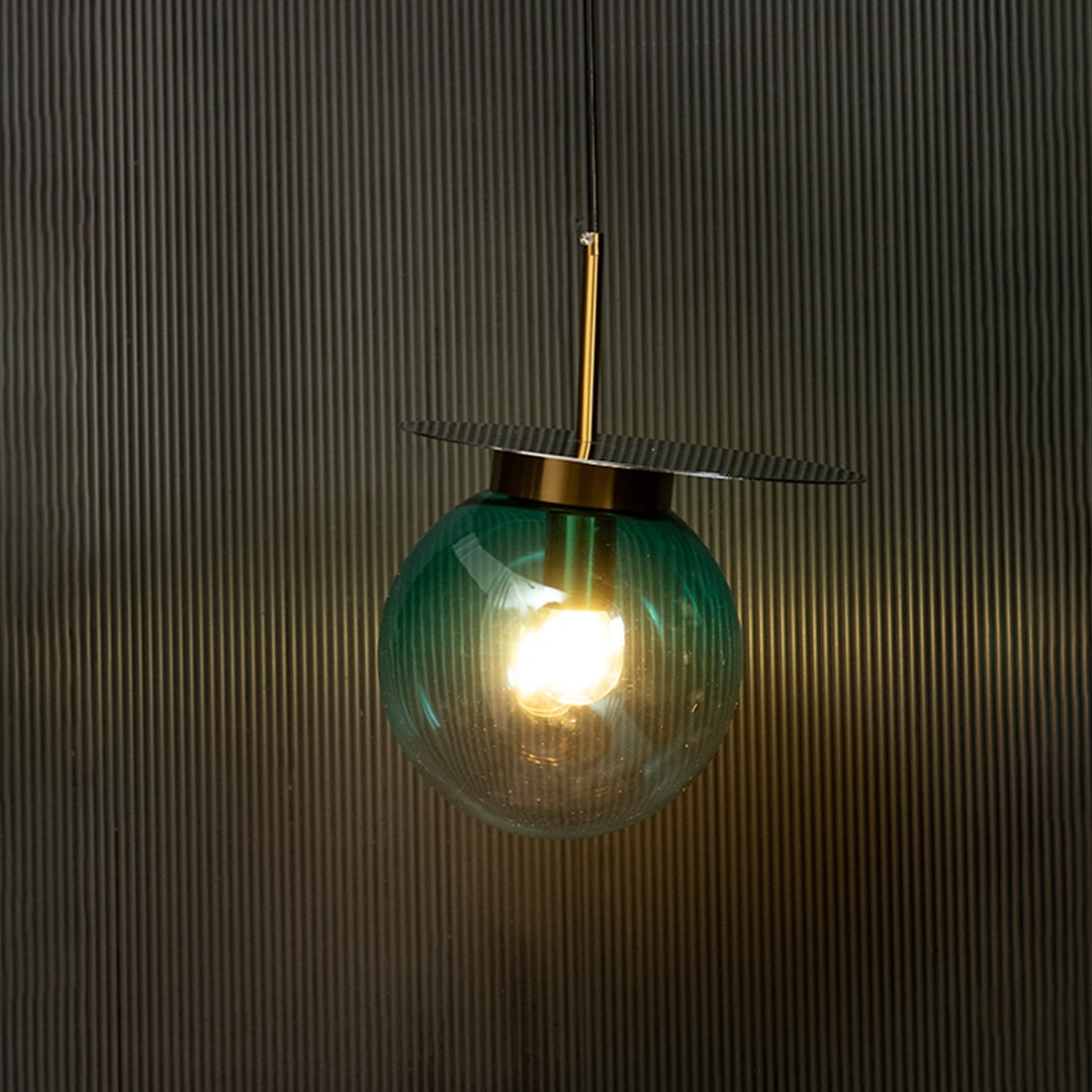 Elegant blue glass pendant light illuminated against dark background highlighting refined glass finish and gold craftsmanship.