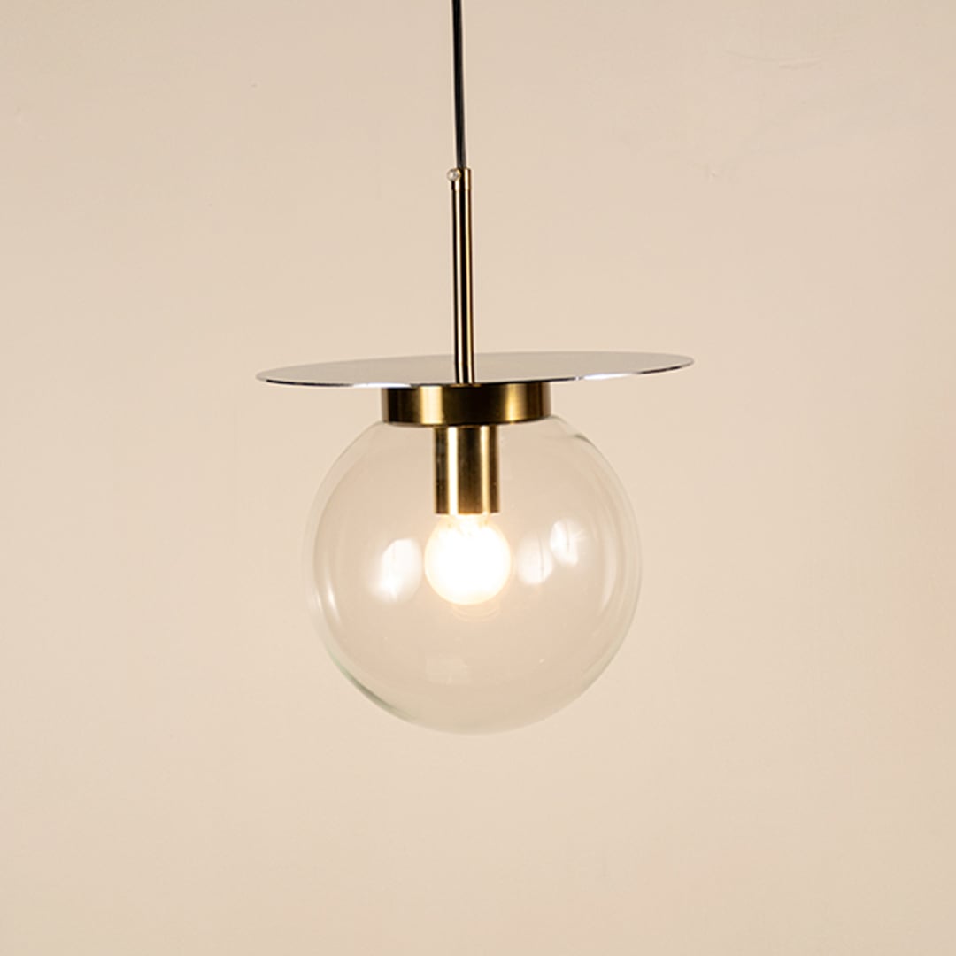 Clear glass pendant light with gold holder glowing softly on white background creating modern ambience for modern living and dining rooms.