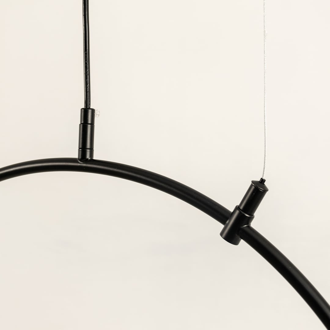 Close up of a black curved ceiling light frame with two slim hanging wires attached shown against a light background.