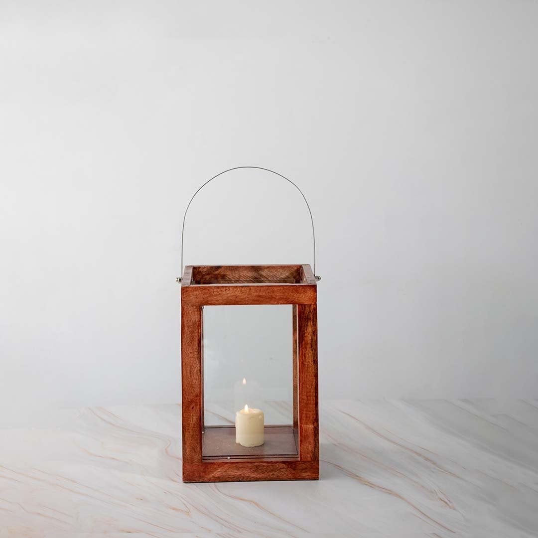 Wooden lantern with stainless steel handle and glass panels on a clean white background with candle glowing inside.