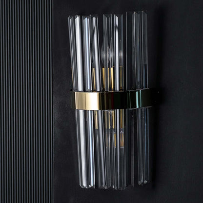 Crystal wall light with the light on against a black background creating a dramatic glow that enhances the reflective glass rods and golden band.