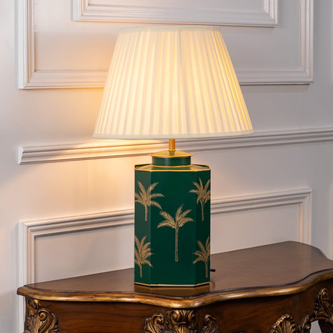 Stylish table lamp with pleated white shade and green ceramic base adorned with delicate palm motifs and gold finished edges.